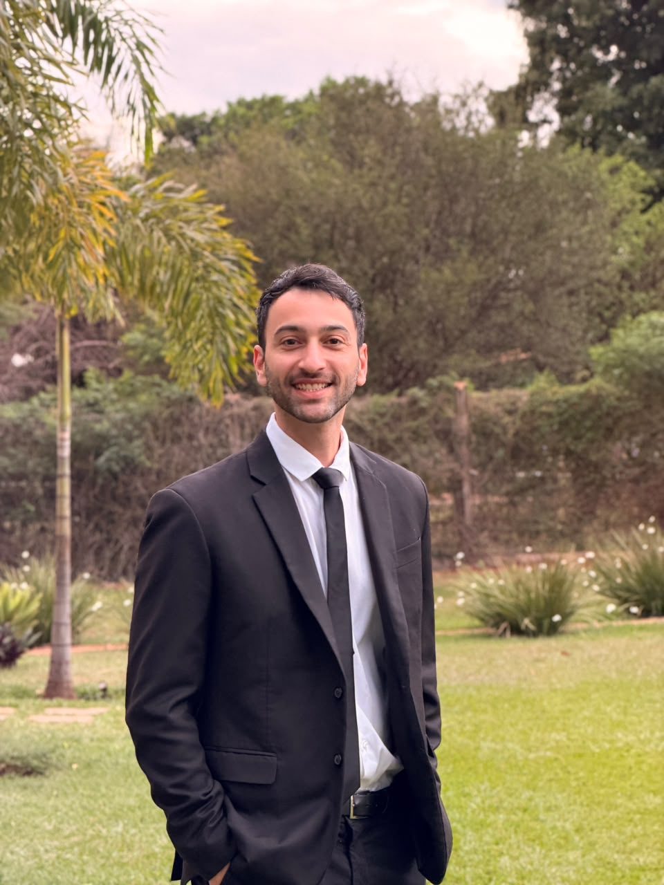 Caio Panissi, de terno escuro, sorrindo em um jardim
